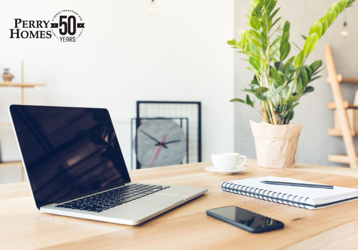 Laptop sitting on a table with a pen, notebook, coffee mug and plant